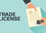 Illustration of a person stamping a trade license document on a teal background with bold 'TRADE LICENSE' text beside it.